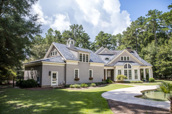 A large cape cod style home with columns and windows and a round porch patio